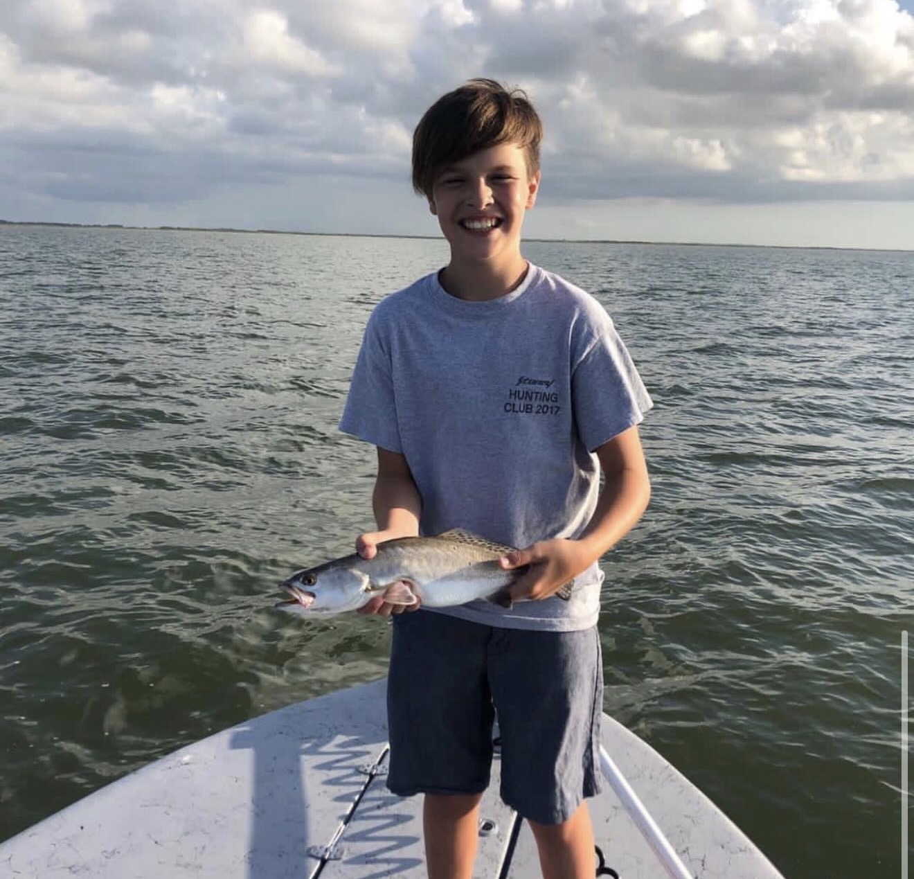 Kid holding a Galveston Bay trout on the bow of the skiff at sunset